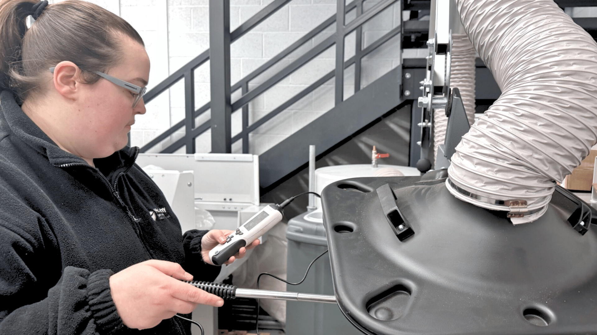 Person measuring airflow from a large vent hose in an industrial setting.