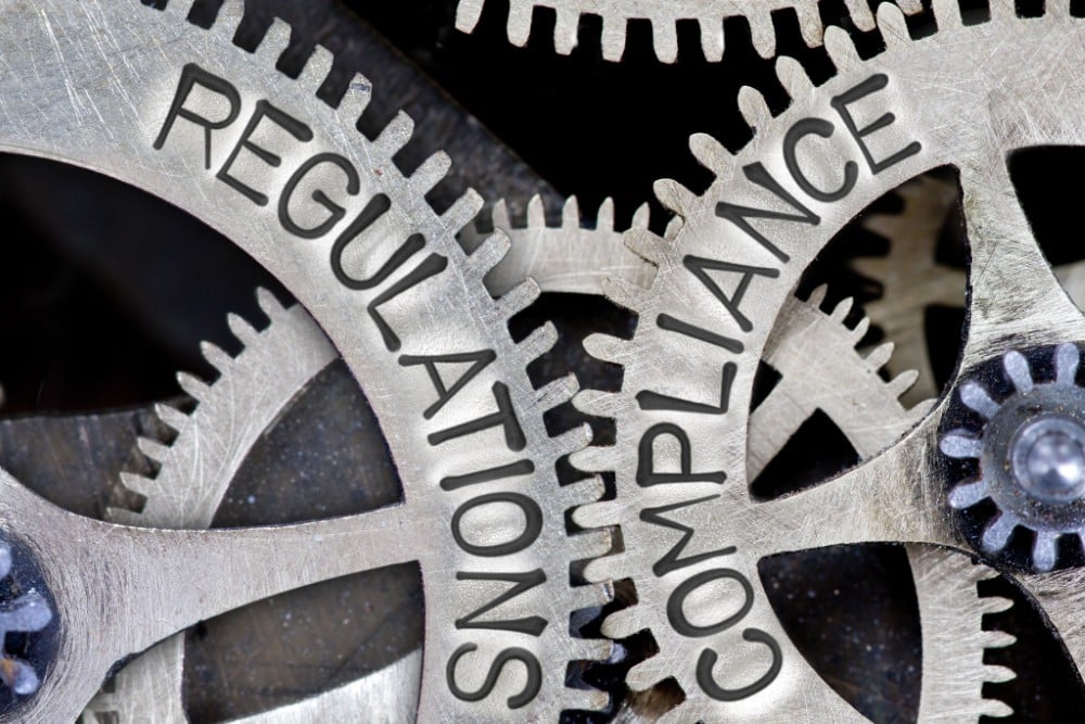 Two interlocking gears labeled "Regulations" and "Compliance" in close-up view.