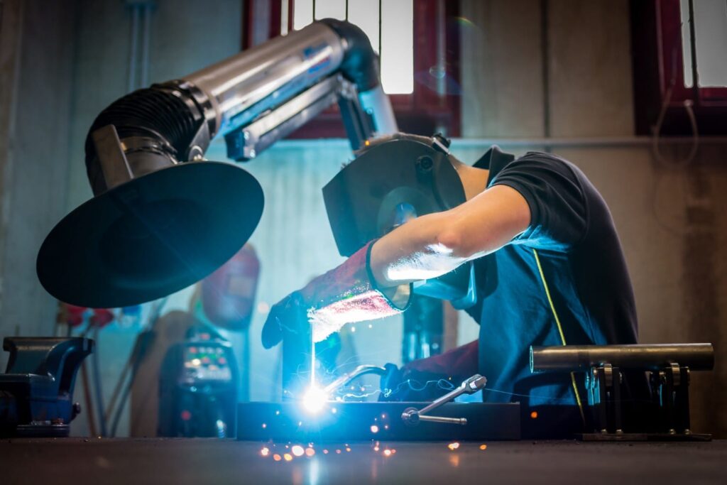 A person welding metal, wearing protective gear, in an industrial workshop.