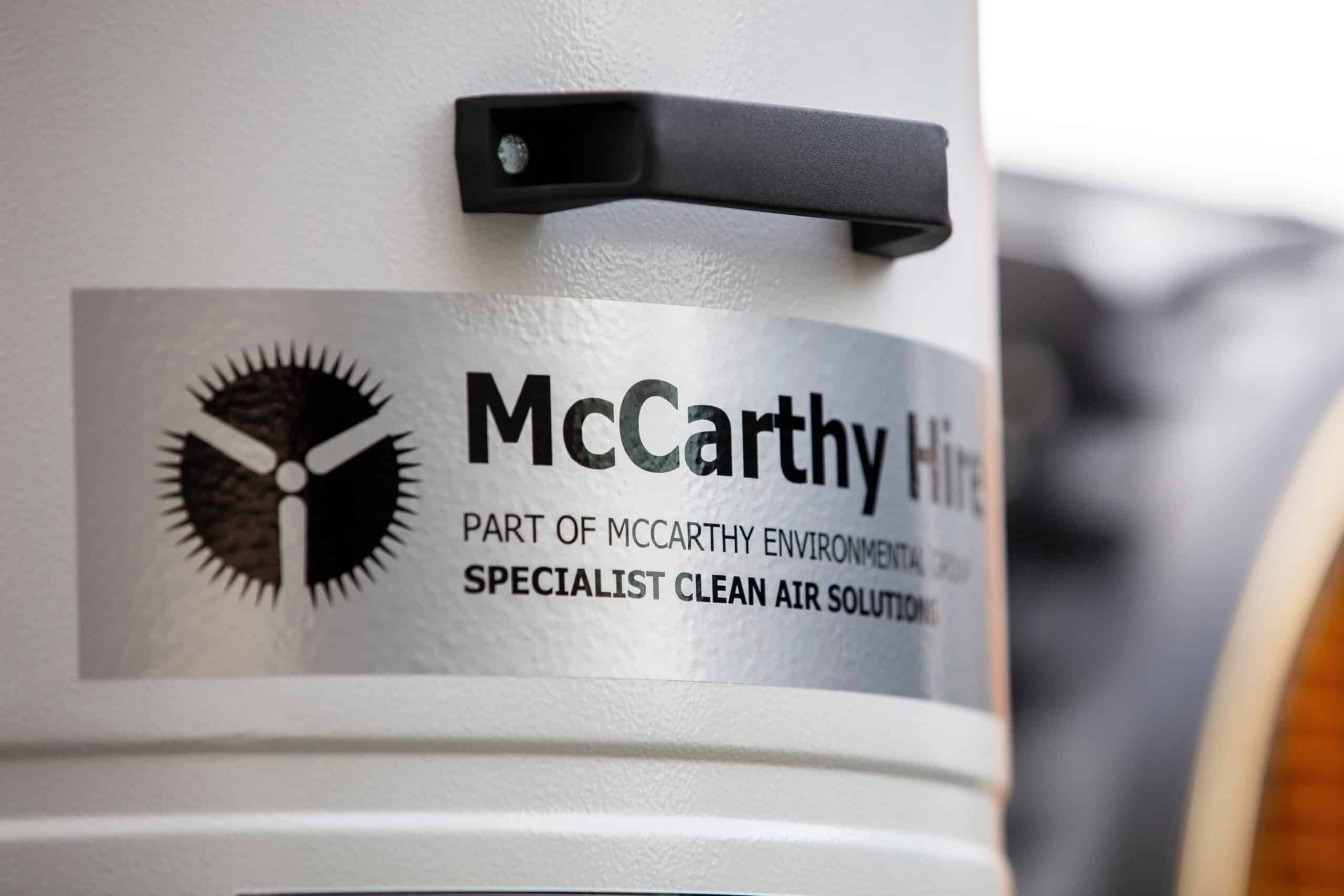 A person measures airflow with a digital anemometer inside a large industrial vent.